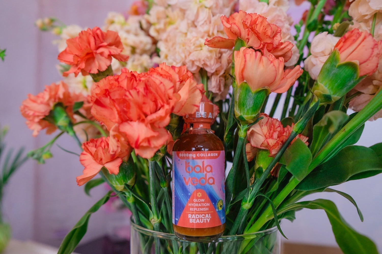 Image of radical beauty collagen shot in front of a vase of flowers