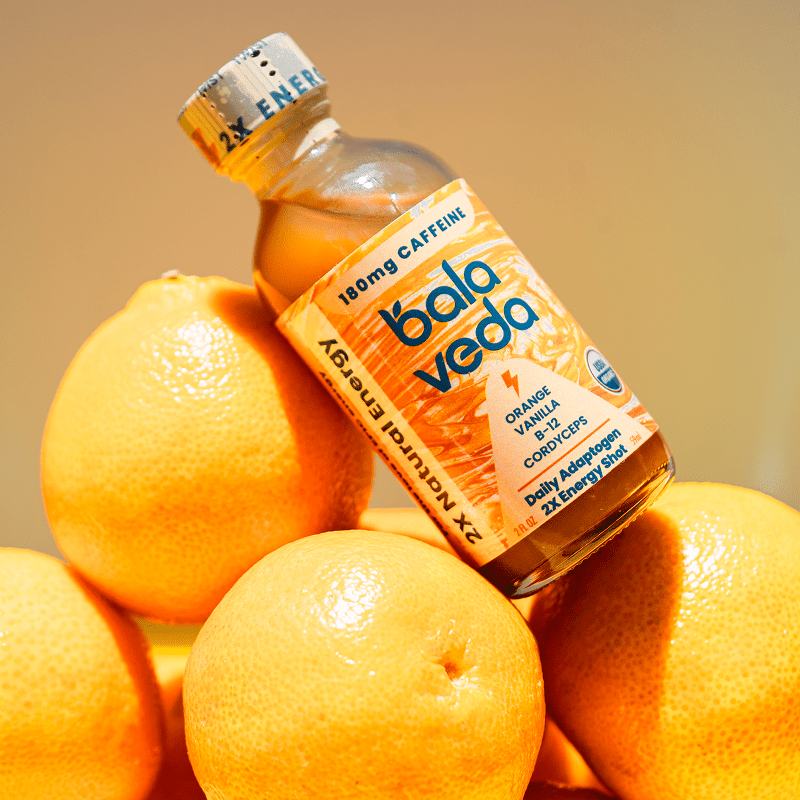 balaveda Supersonic Citrus 2x Energy Shot in yellow glass bottle on top of lemons with a yellow background.