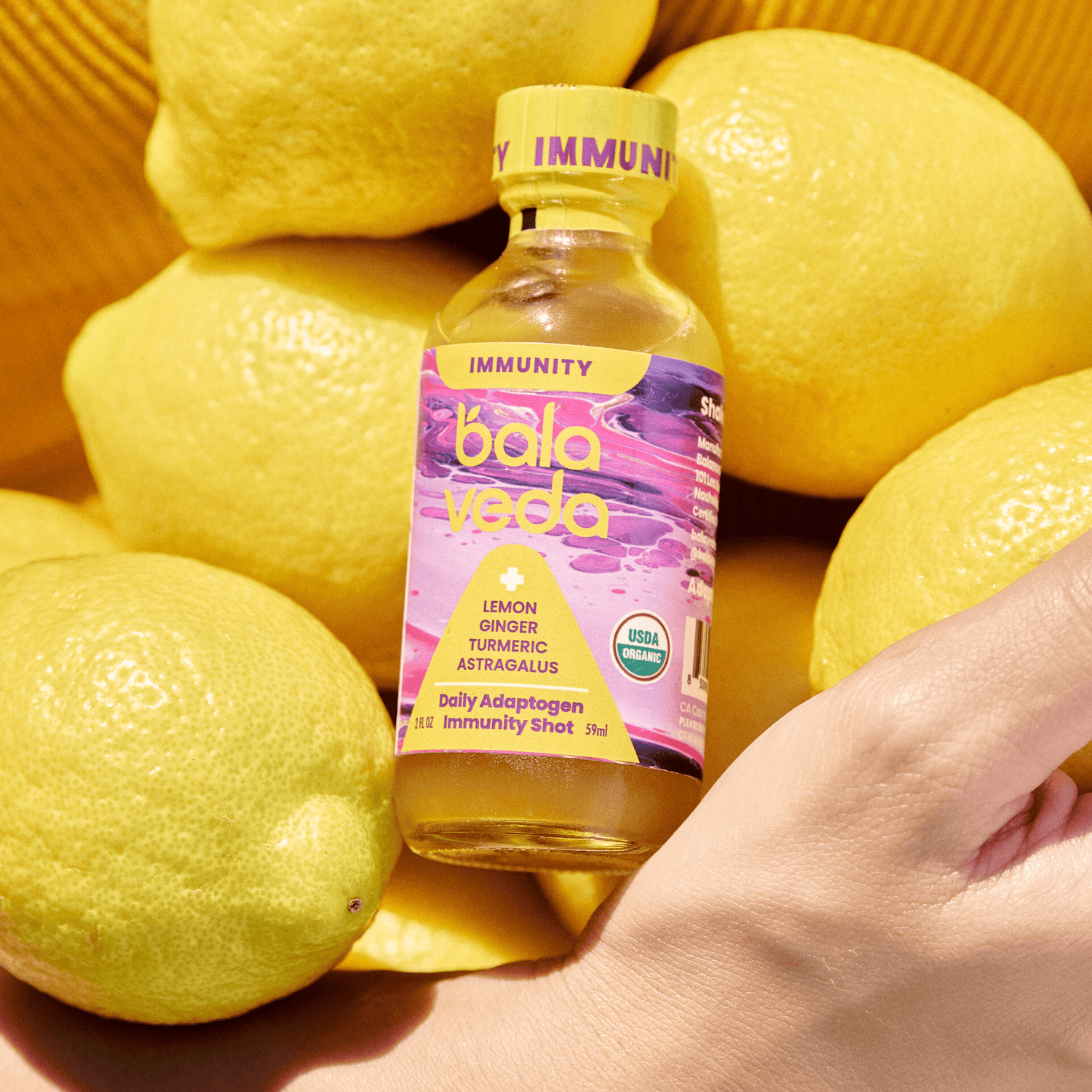 Balaveda Totally Turmeric and lemon Immunity Shot in yellow and pink glass bottle with lemons in the background.