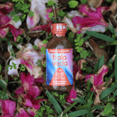 Bala Veda radical beauty shot bottle surrounded by flowers and greenery.
