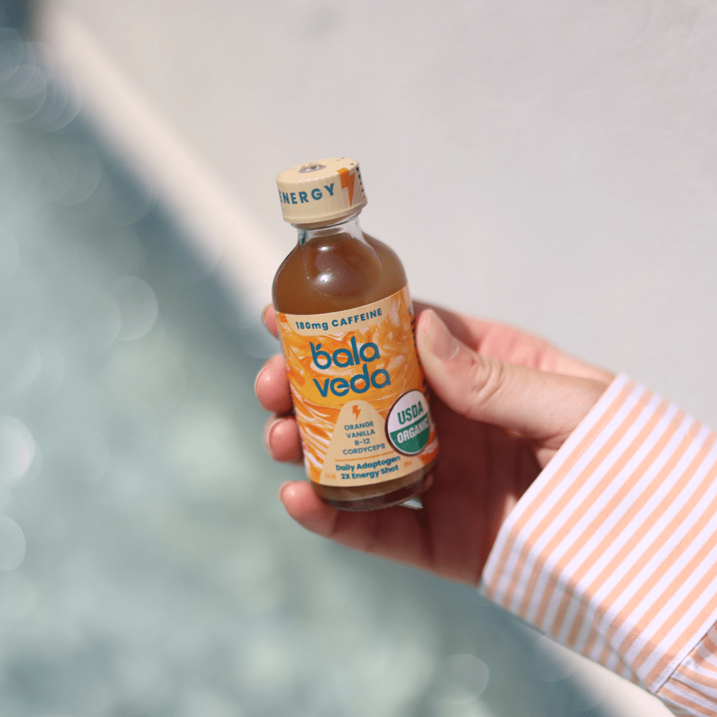 Hand holding a bottle of Bala Veda supersonic citrus energy drink with a blurred background
