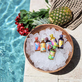balaveda immunity, beauty, and energy shot samplers in bowl on ice, beside a pool, a pineapple, and red flowers
