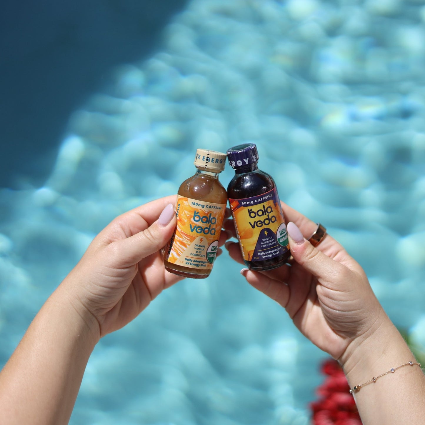 Two bottles of Bala Veda energy drink products held by a person with a pool in the background