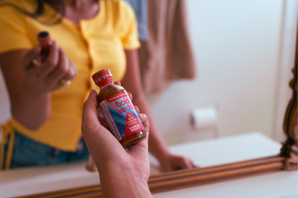 Person holding a bottle of balaveda beauty collagen shot in front of a mirror.