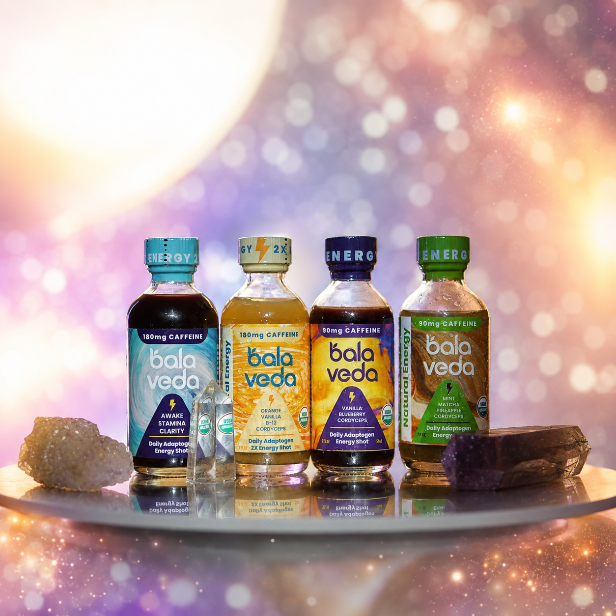 Four bottles of balaveda energy drinks on a reflective surface with a blurred, colorful background.