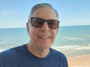 John wearing sunglasses with a beach and ocean view in the background